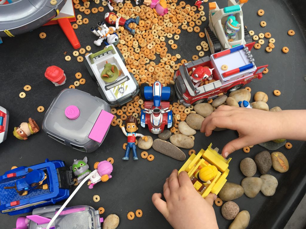 I helped them place the stones in the tuff spot, along with some of their Paw Patrol toys. Then poured some of the cereal into a container. This is what it looked like.